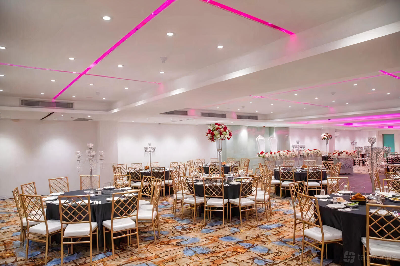 An event venue with round tables, gold chairs, floral centerpieces, and pink LED ceiling lights at Stars Palace.