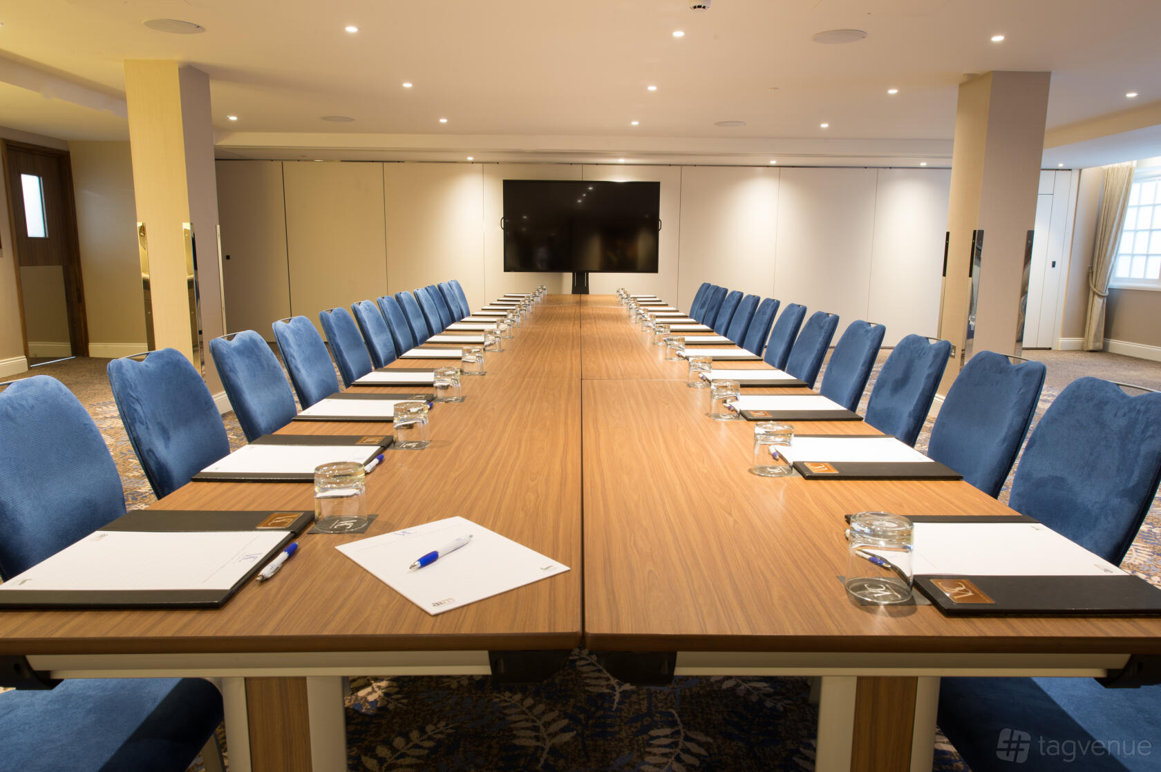 An event space with a long conference table, blue upholstered chairs, and a large screen at Victory Services Club.