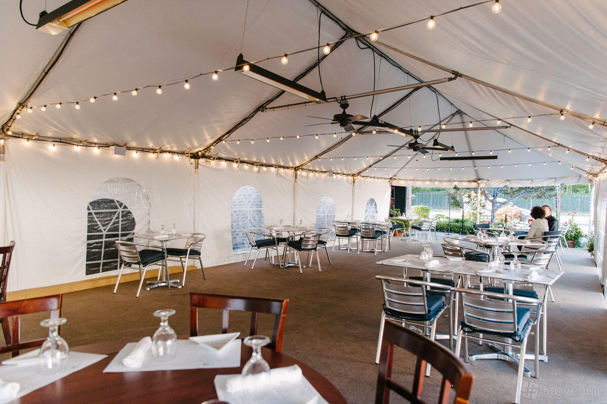 An outdoor restaurant seating area under a large tent with string lights and metal tables at Il Luogo Ristorante.