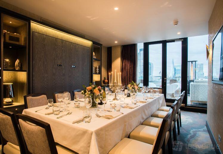 A dining room with floor-to-ceiling windows, set table with white linens, and city views at Aviary Rooftop Bar & Restaurant.