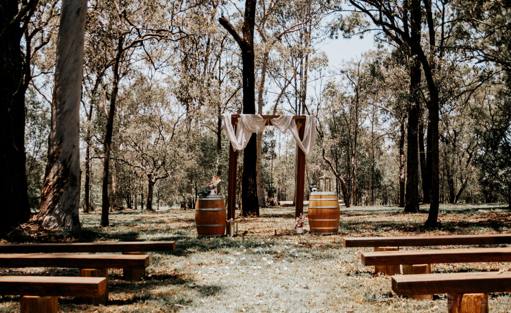 An outdoor garden with wooden benches, draped arbor, and wine barrel accents at Woodstock Farm Tamborine.