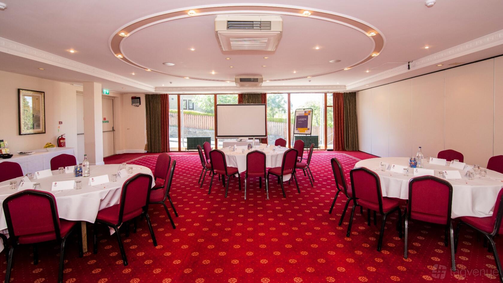 An event space in a hotel with round tables, red chairs, and a large window at The Craiglands Hotel.