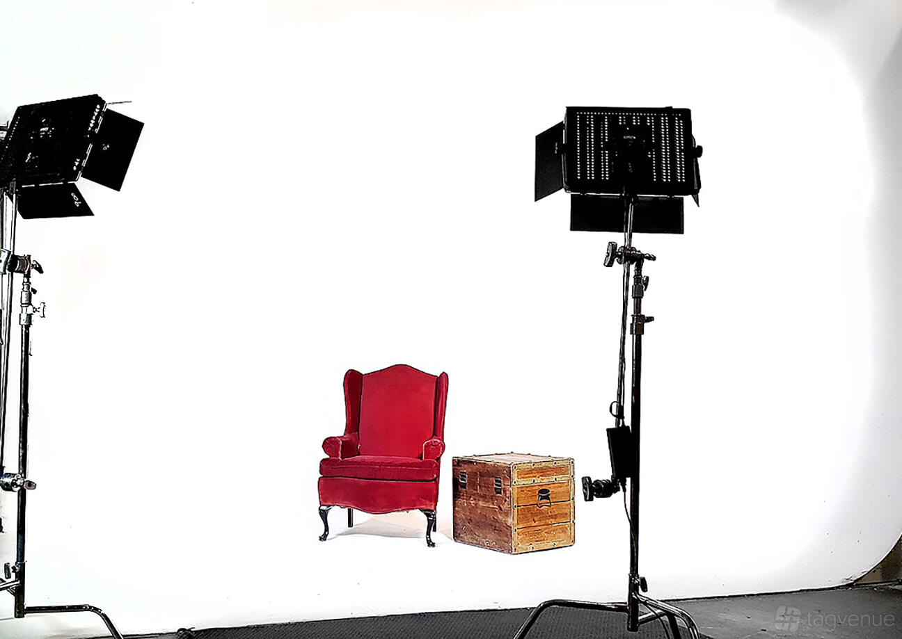 A photo studio with a seamless white backdrop, red armchair, wooden trunk, and studio lights at Studio II at the Brewery Arts Complex.