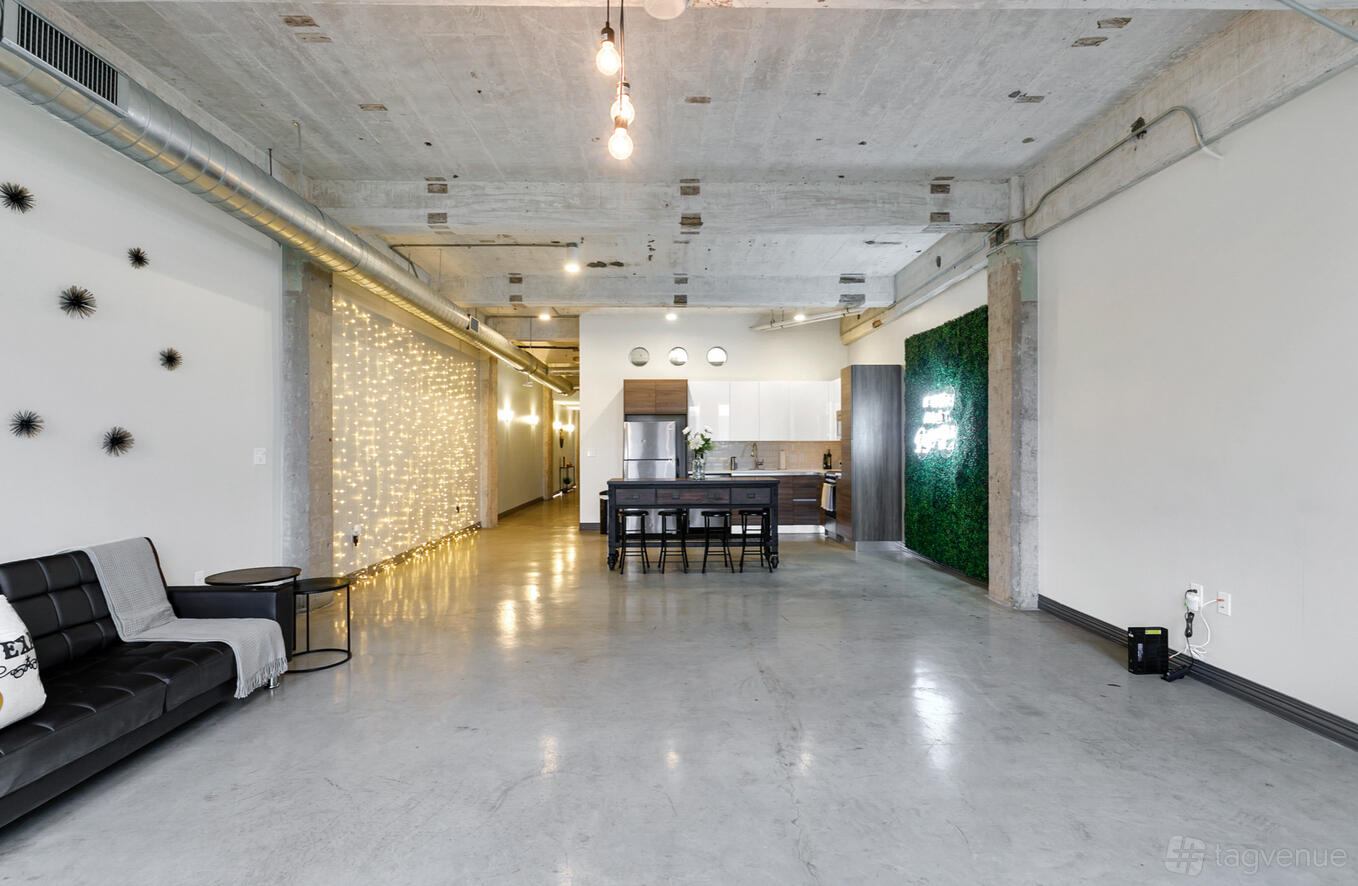 An open event venue with polished concrete floors, exposed ceiling, string lights, and a kitchenette at L.A.Y.D Spaces @ Harry Hines.