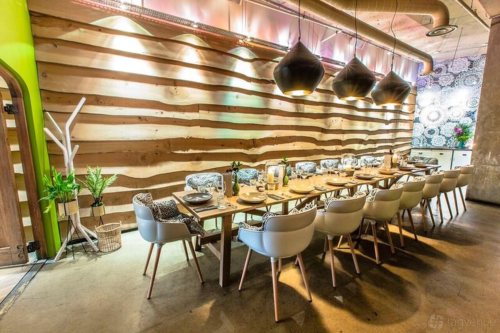A dining room with a long wooden table, modern white chairs, pendant lights, and a wavy wood accent wall at The Folly.