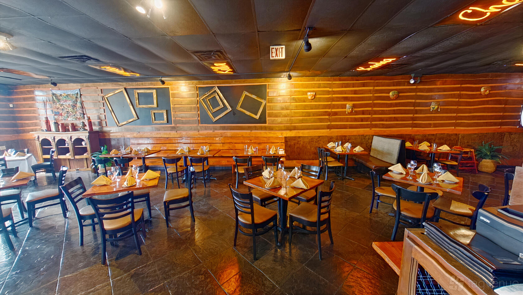 A restaurant with slate tile floors, wooden walls, framed art, and neatly set tables at Lima Taverna.
