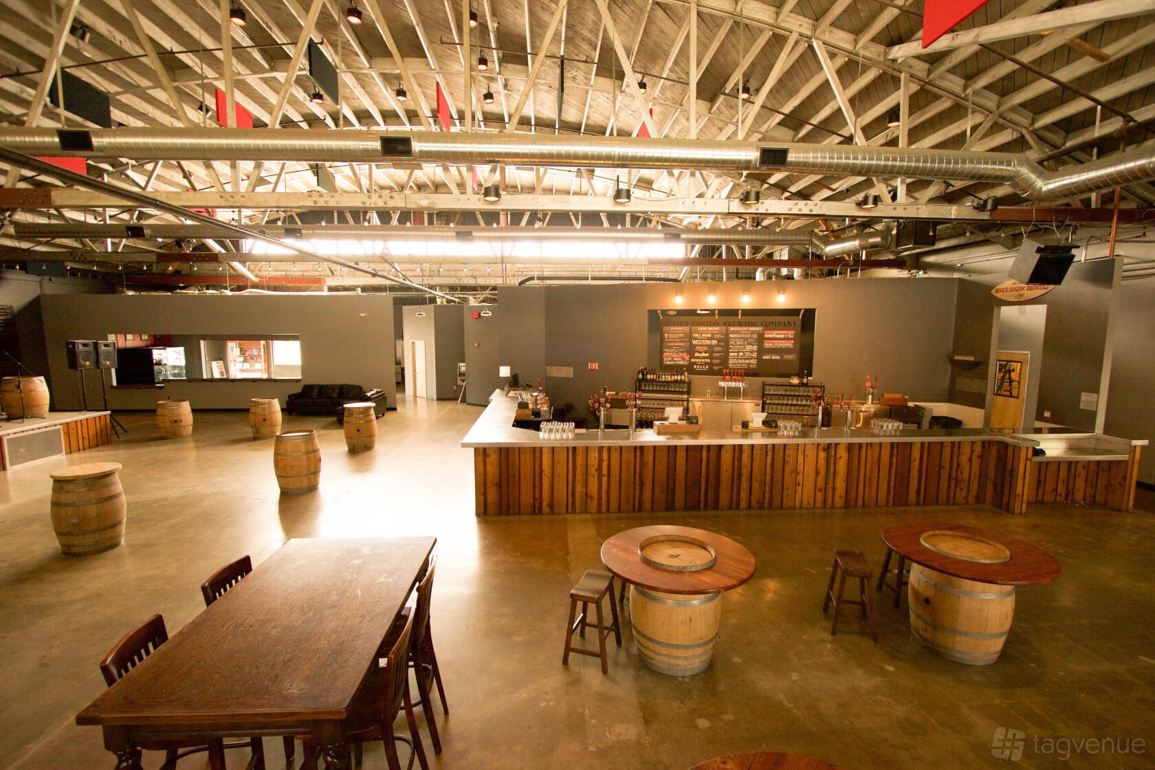 A spacious warehouse hall with exposed beams, barrel tables, and a wooden bar at Devil's Canyon Brewing Company.