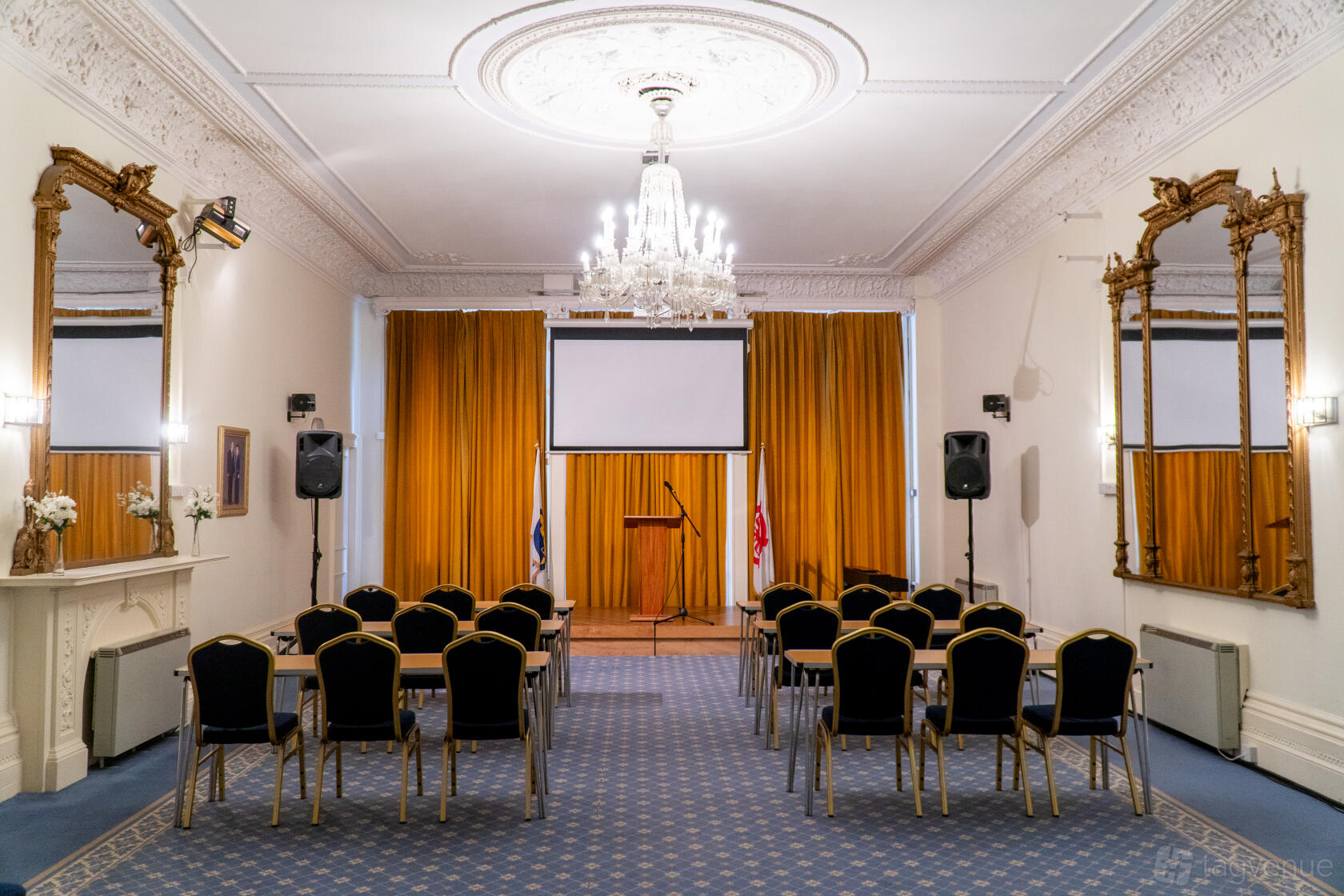 An event venue with a crystal chandelier, ornate mirrors, and gold curtains behind a podium at 43LG Conference and Events Venue.