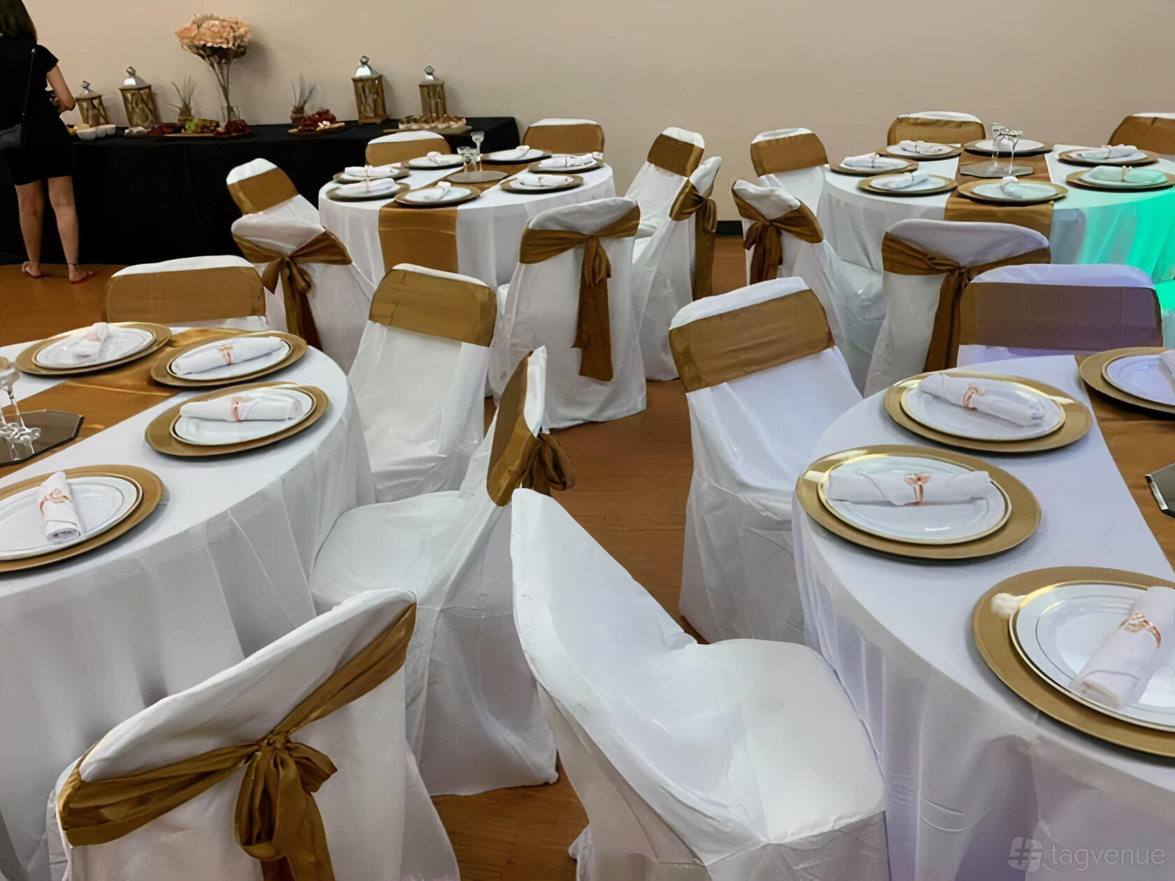 An event venue with round tables covered in white linens and gold chair sashes at Magnolia Event Space.