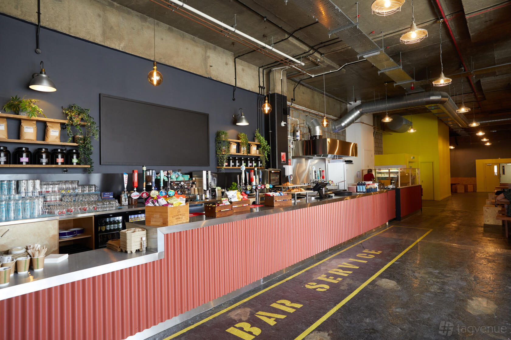 An event venue bar with a long corrugated metal counter, exposed ductwork, and industrial decor at Archives London.