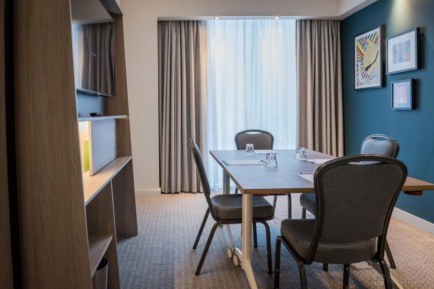 A hotel meeting room with a rectangular table, four chairs, and floor-to-ceiling windows at Hampton by Hilton Manchester Northern Quarter.