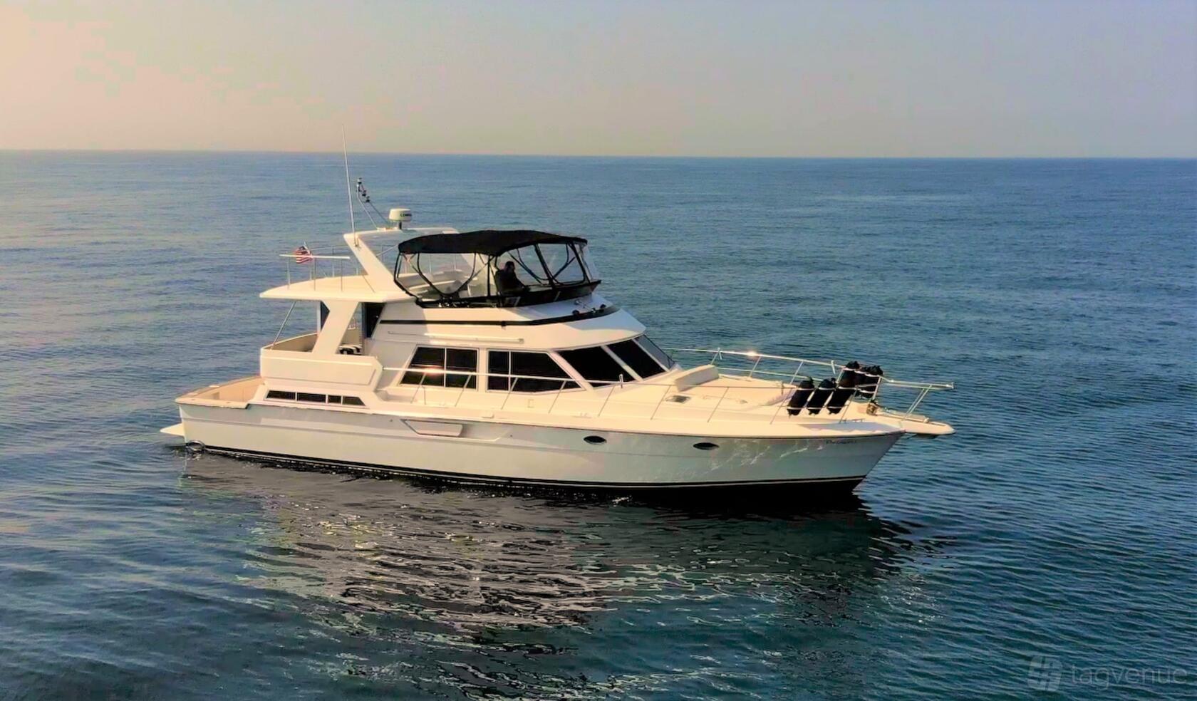 A white yacht with a covered upper deck and open bow cruising on calm ocean waters at Luxury Yacht Charter.