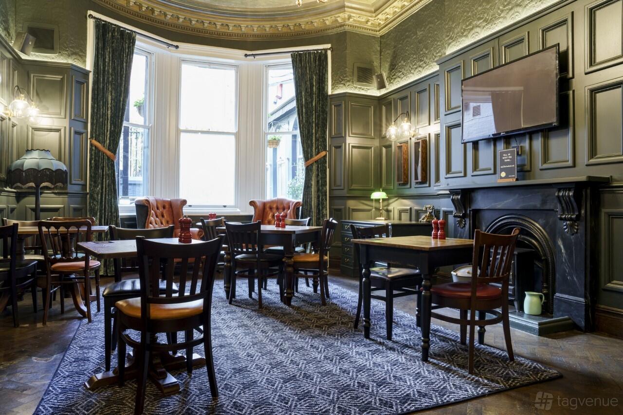 A dining room in a pub with dark wood paneling, upholstered armchairs, and a fireplace at Old Joint Stock.