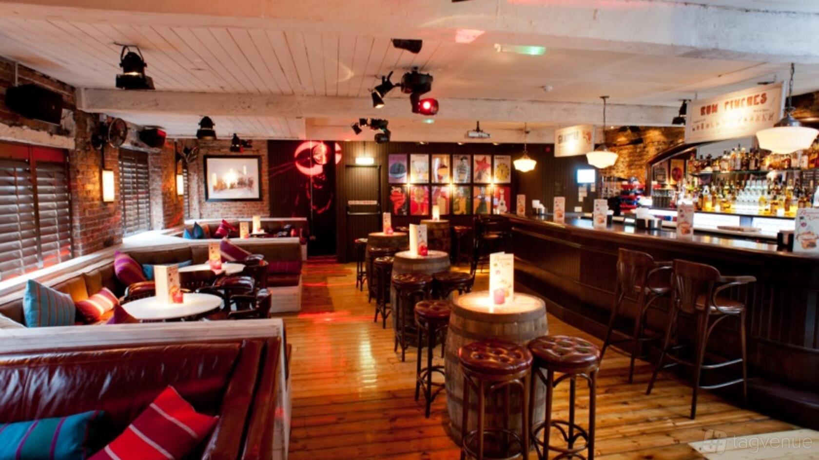 An event space in a bar with exposed brick walls, leather booths, round tables, and barrel high-tops at Revolution Leeds Call Lane.