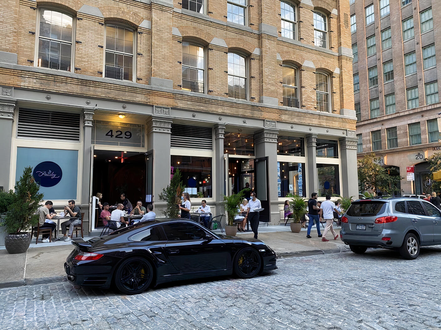 A restaurant with outdoor sidewalk seating, potted plants, and large windows at Paisley.