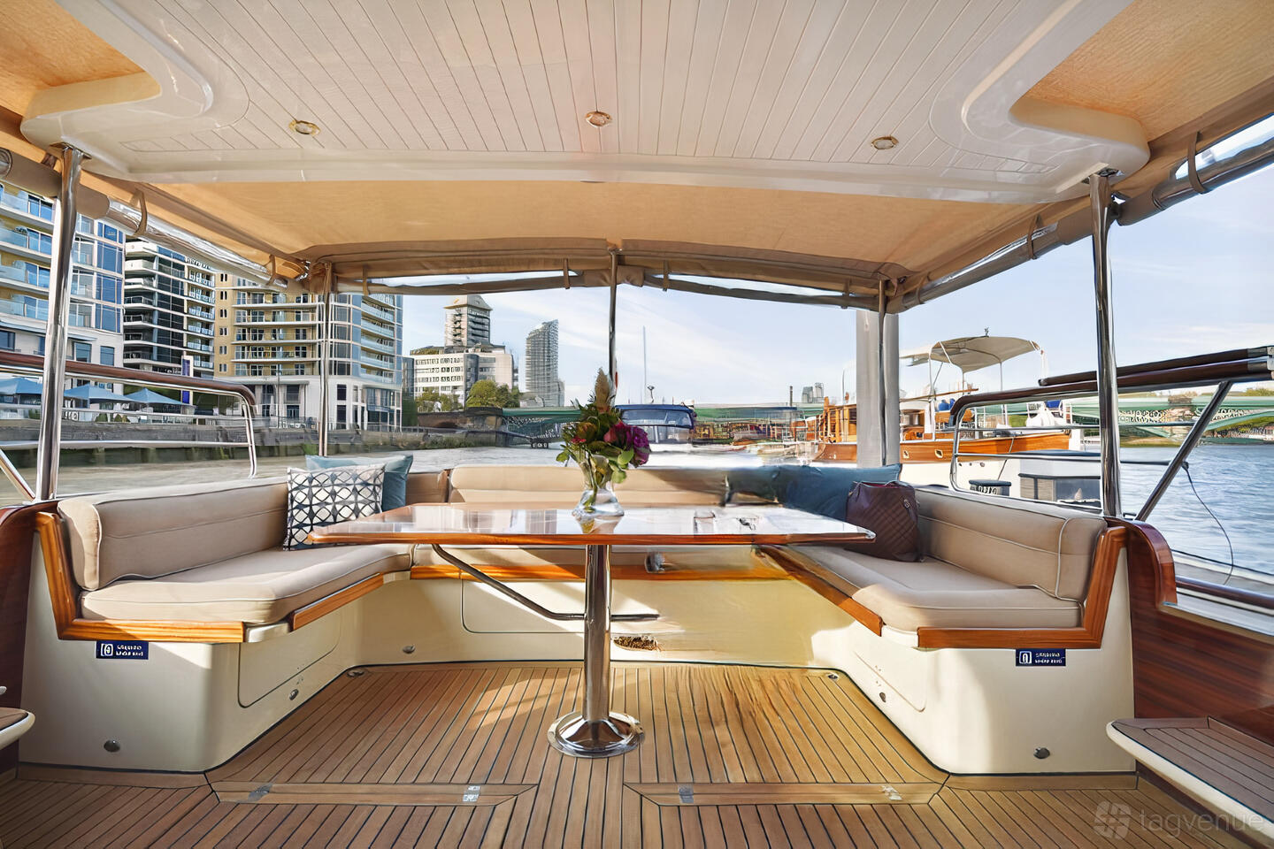 A yacht lounge with cushioned bench seating, a wooden table, and water views at Thames Limo.