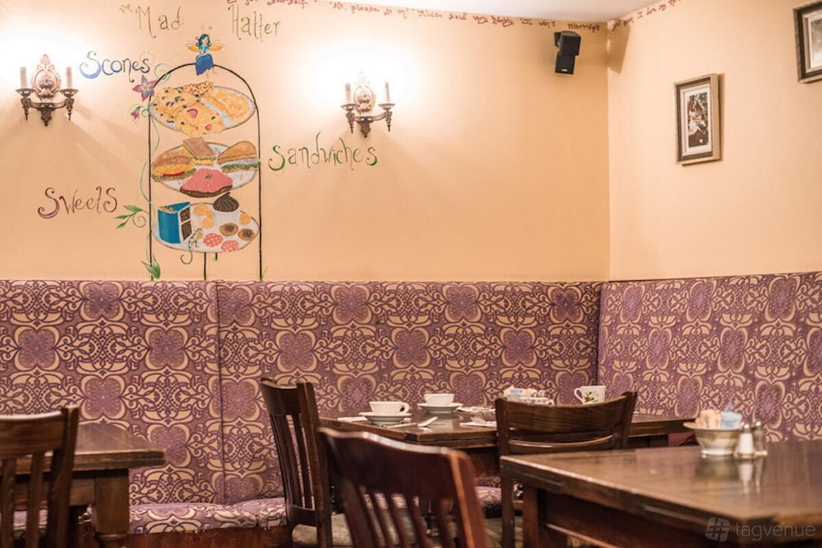 A cafe dining room with patterned purple banquette seating, wooden tables, and whimsical wall art at Alice's Tea Cup Chapter 1.
