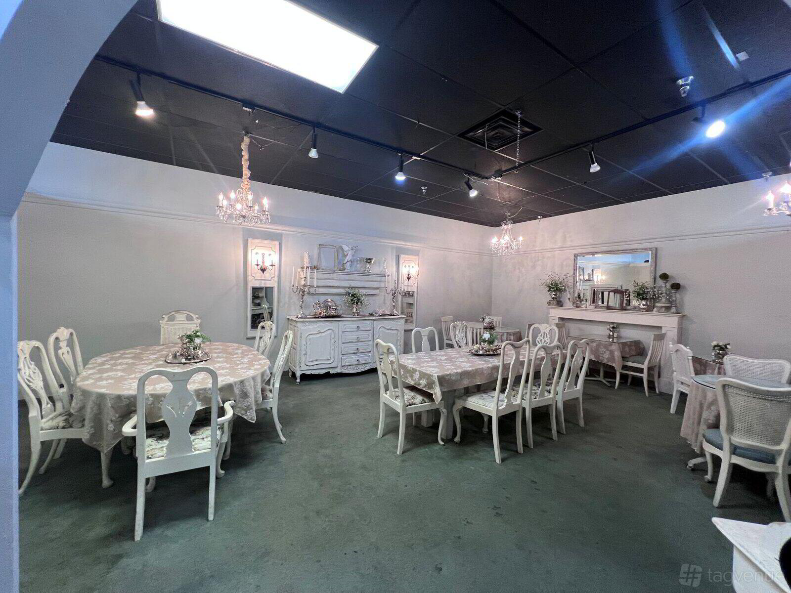 A tea room with white vintage-style tables and chairs, chandeliers, and a buffet cabinet at Chocolate Angel Cafe & Tea Room - High Street.