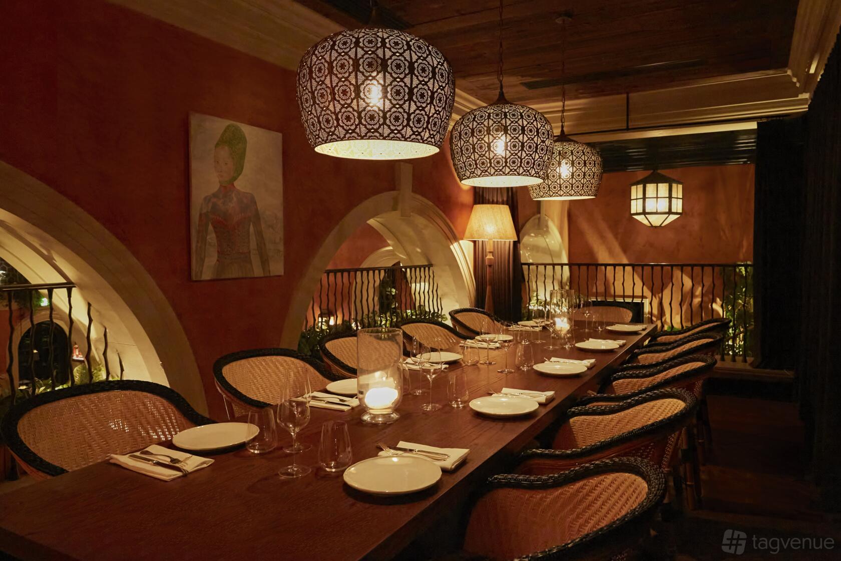 A dining room with rattan chairs, a long wooden table, and patterned pendant lights at Belvedere.