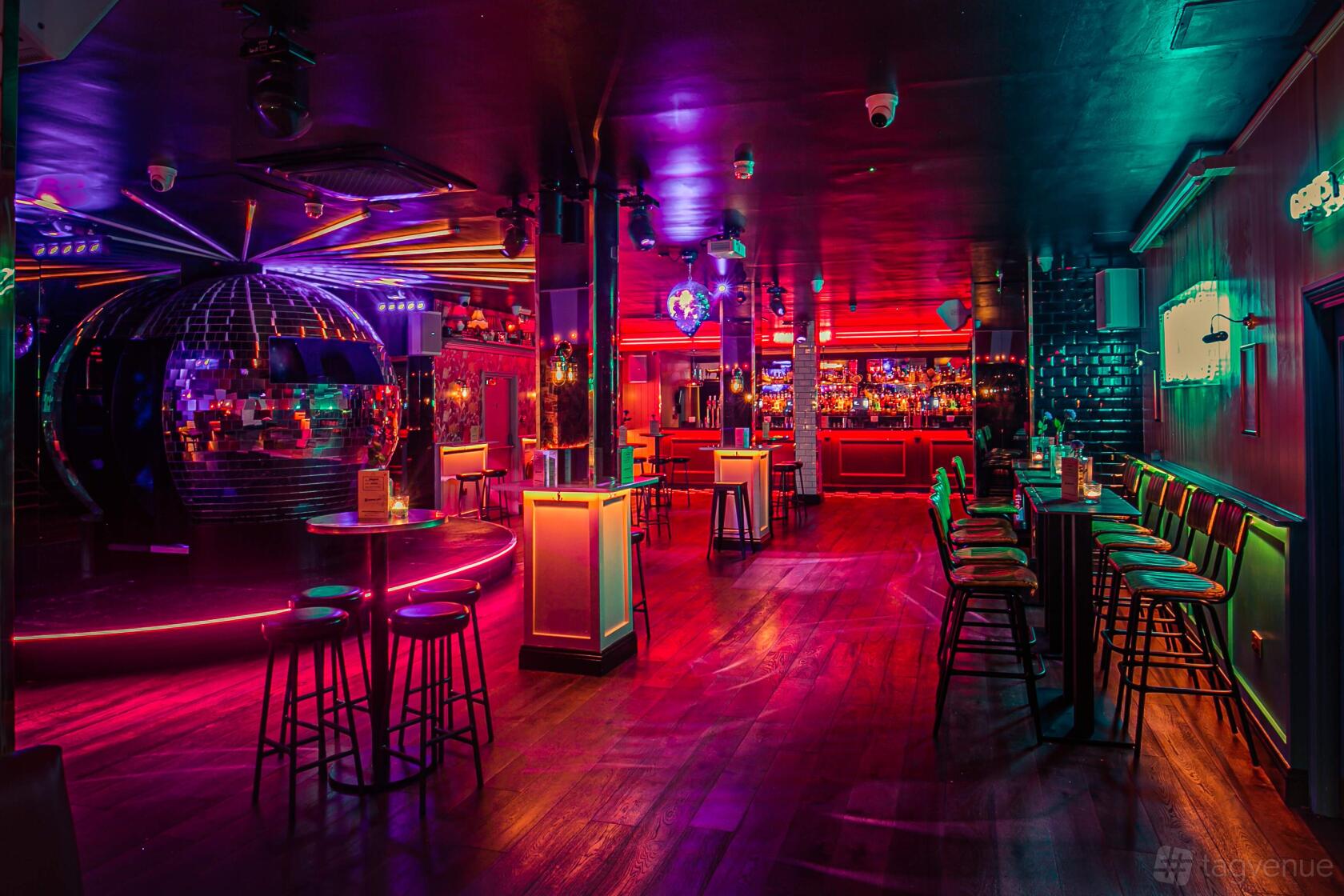 A cocktail bar with neon lighting, a large disco ball, high tables and a colorful bar at Simmons | Holborn.