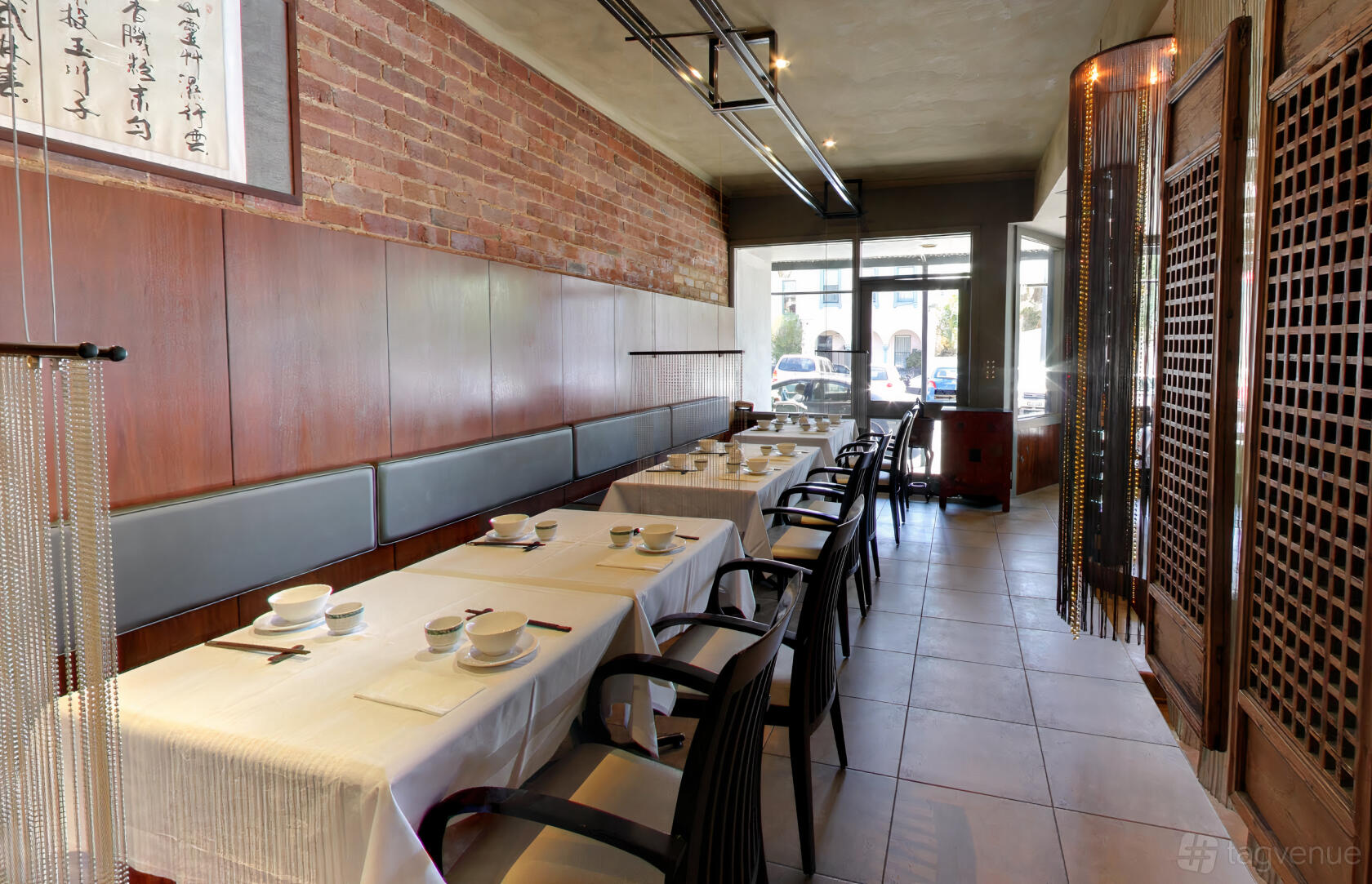 A restaurant with exposed brick walls, wood paneling, and tables with white linens at East Imperial.