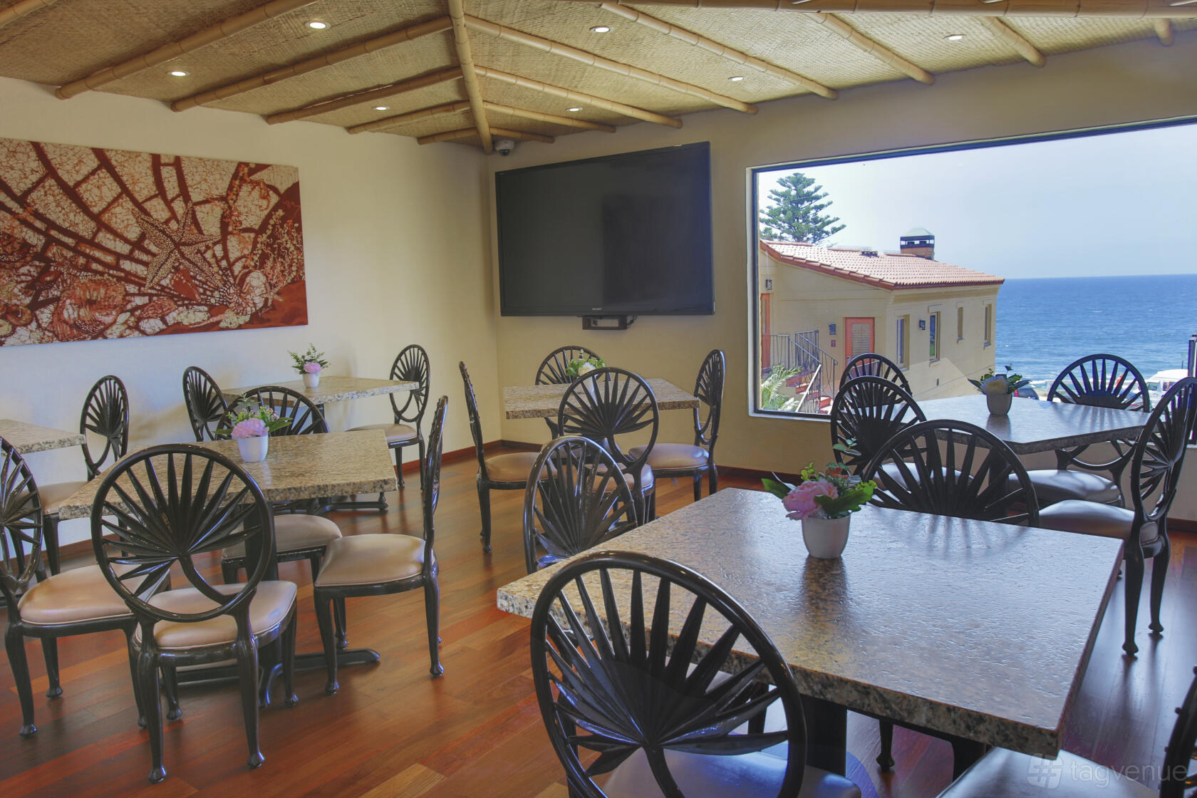 A hotel dining area with granite tables, decorative chairs, and an ocean view window at Pantai Inn.
