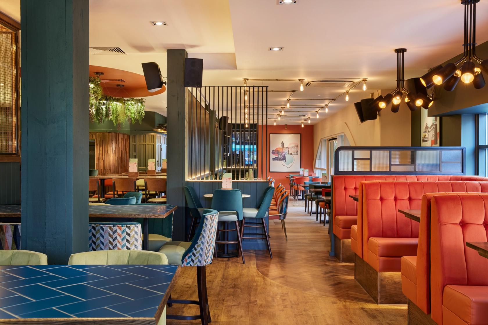 A dining room with orange upholstered booths, teal chairs, and pendant lighting at Pitcher And Piano - Birmingham.
