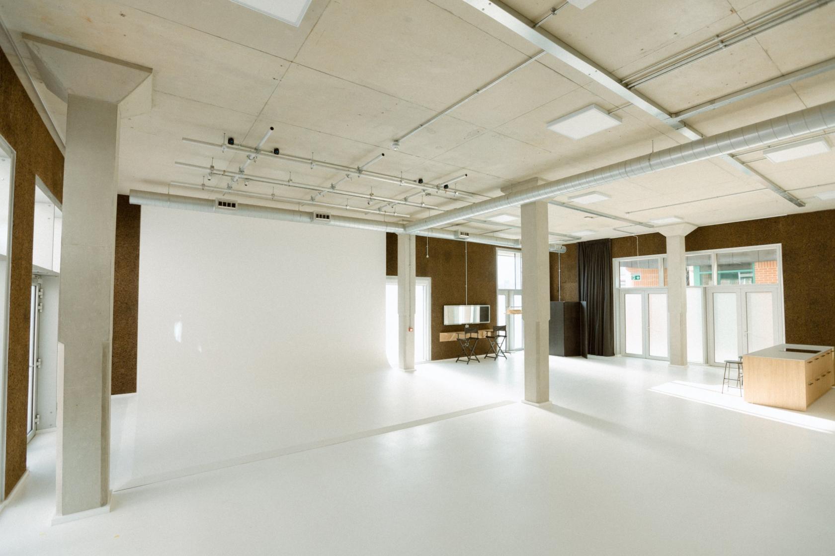 A photo studio with white cyclorama walls, large windows for natural light, and exposed ductwork at Method Studio.