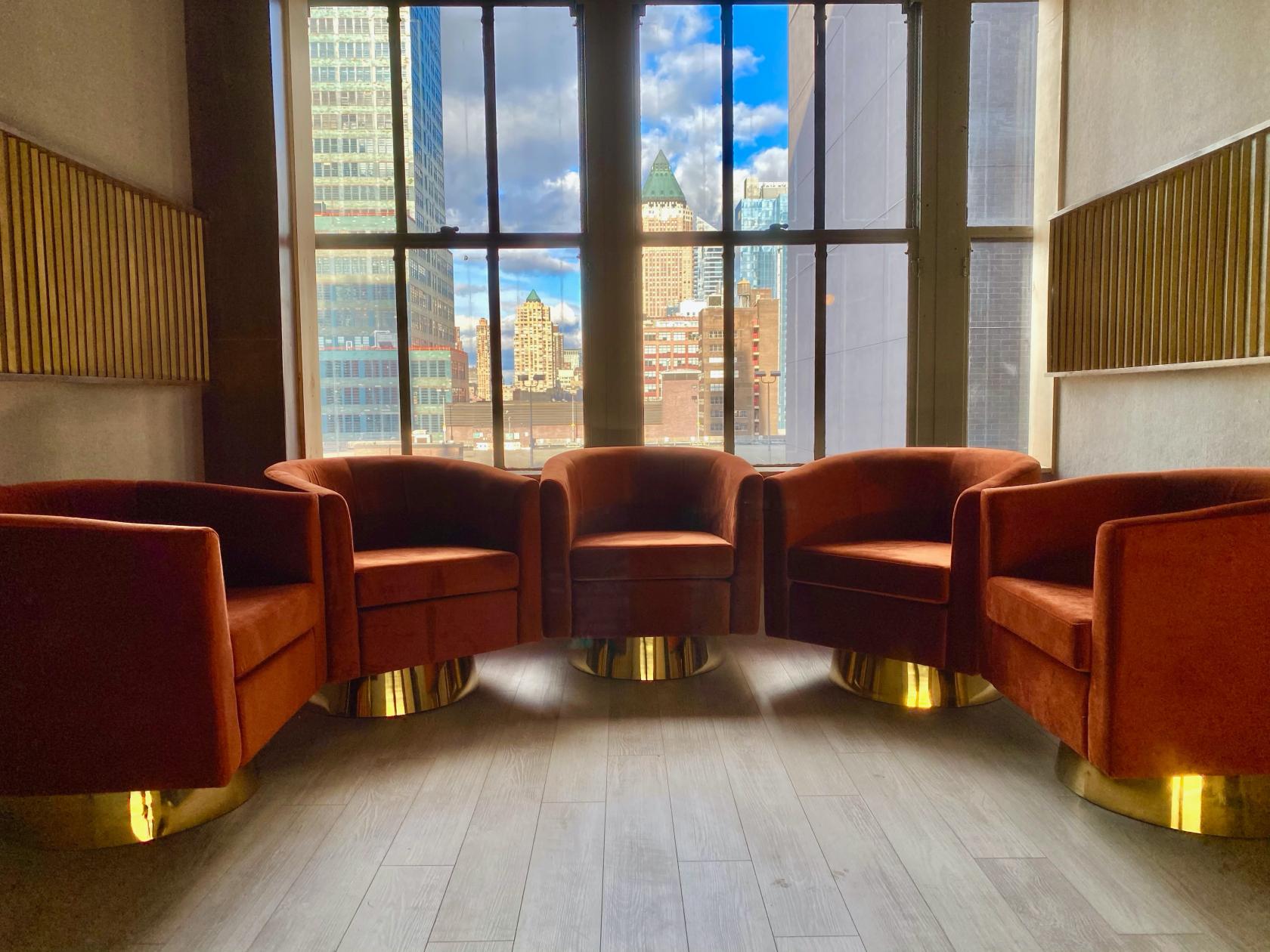A podcast studio with velvet armchairs and floor-to-ceiling windows overlooking city buildings at Lounge Studios NYC.