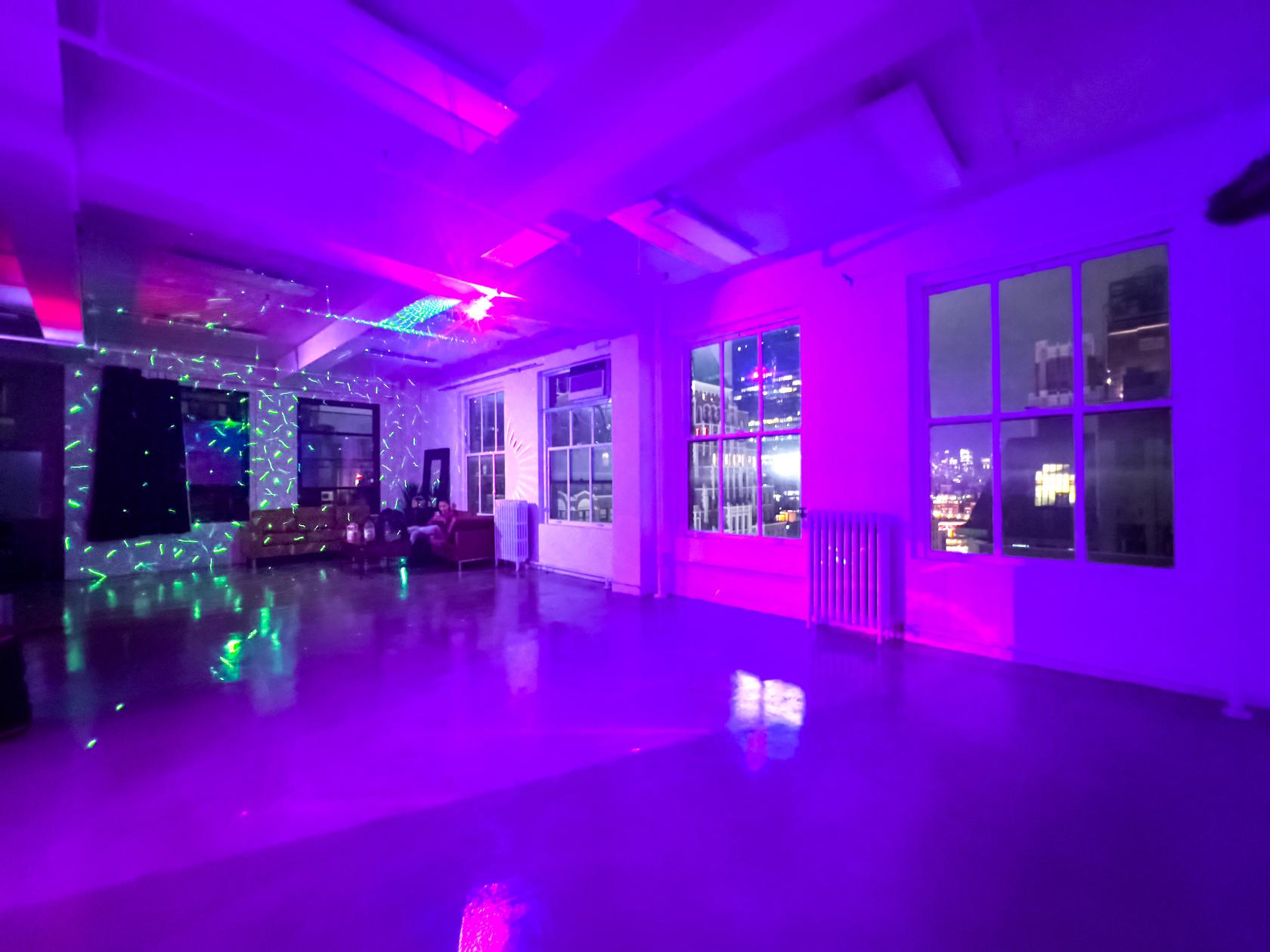 A loft photo studio with colorful LED lighting, polished floors, and large windows showing city views at Event Rental Space Manhattan 23rd Floor.