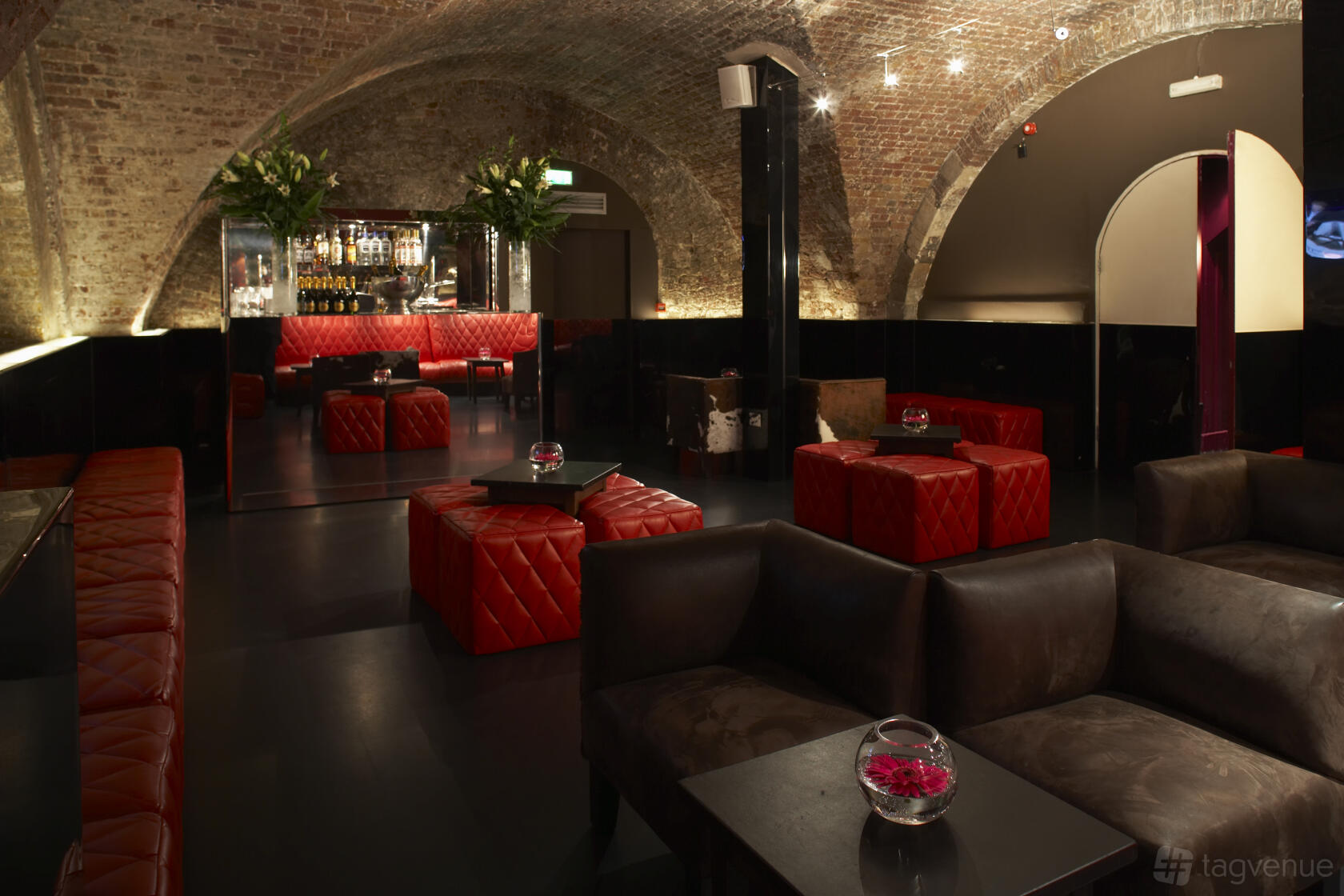 An event venue with vaulted brick ceilings, red quilted seating, and dark leather sofas at Adam House Event Space.