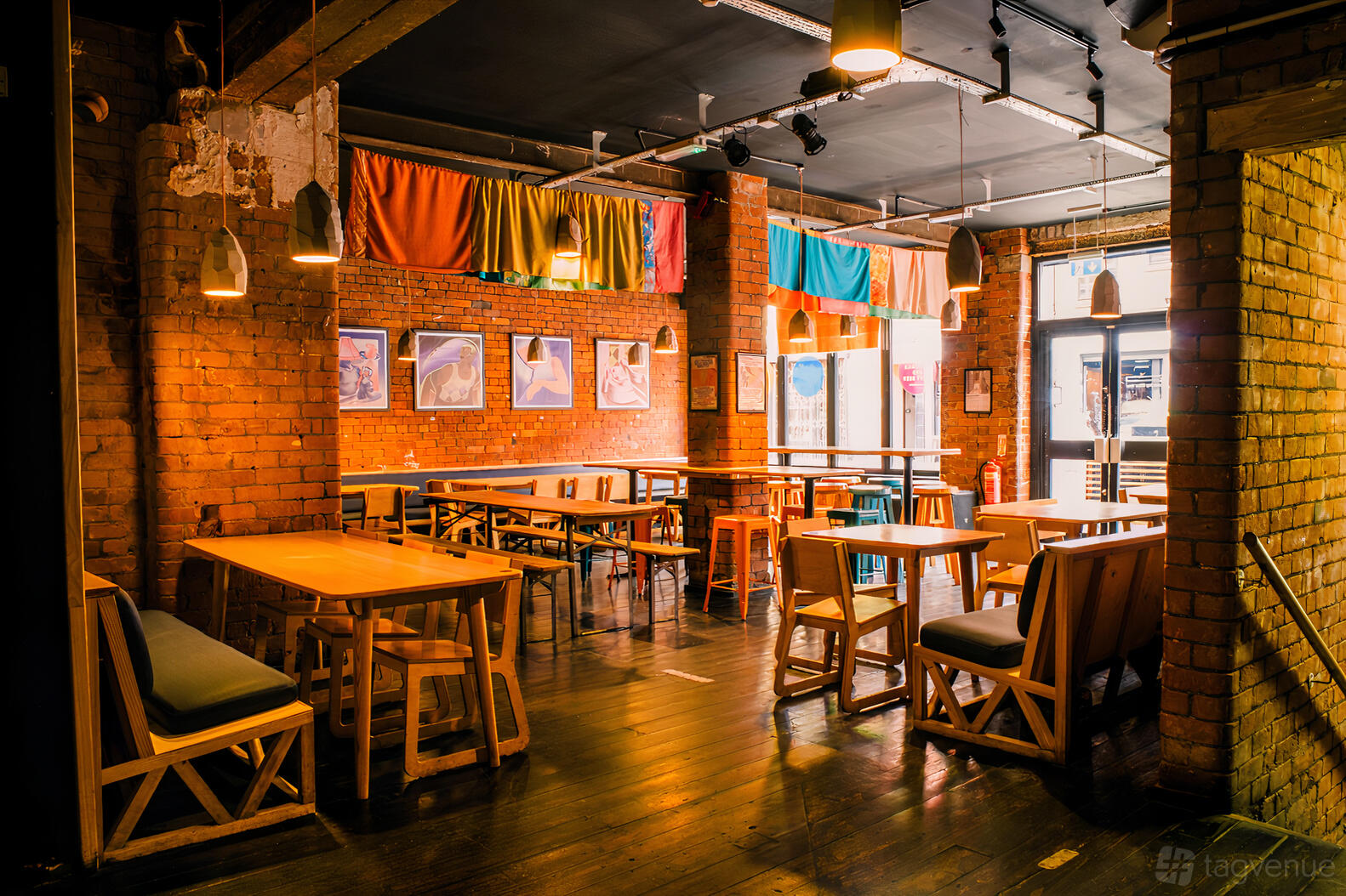 An event space in a bar with exposed brick walls, pendant lights, colorful drapery, and wooden tables at Common.
