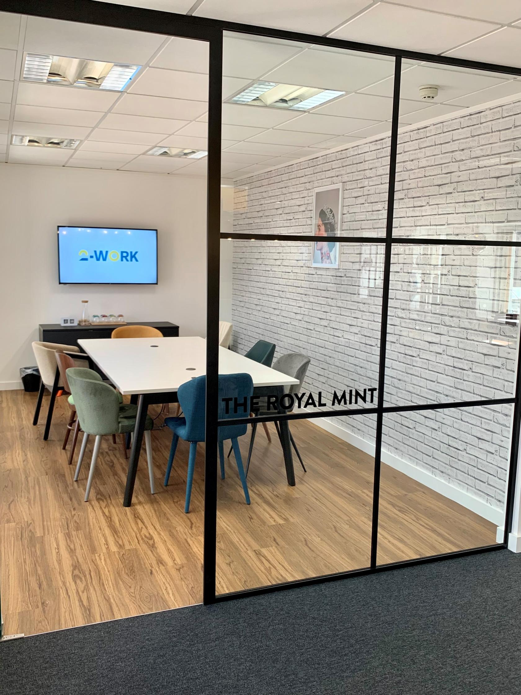 A meeting room with a white table, colorful chairs, brick accent wall, and flat-screen display at 2-Work Bank House Leeds.