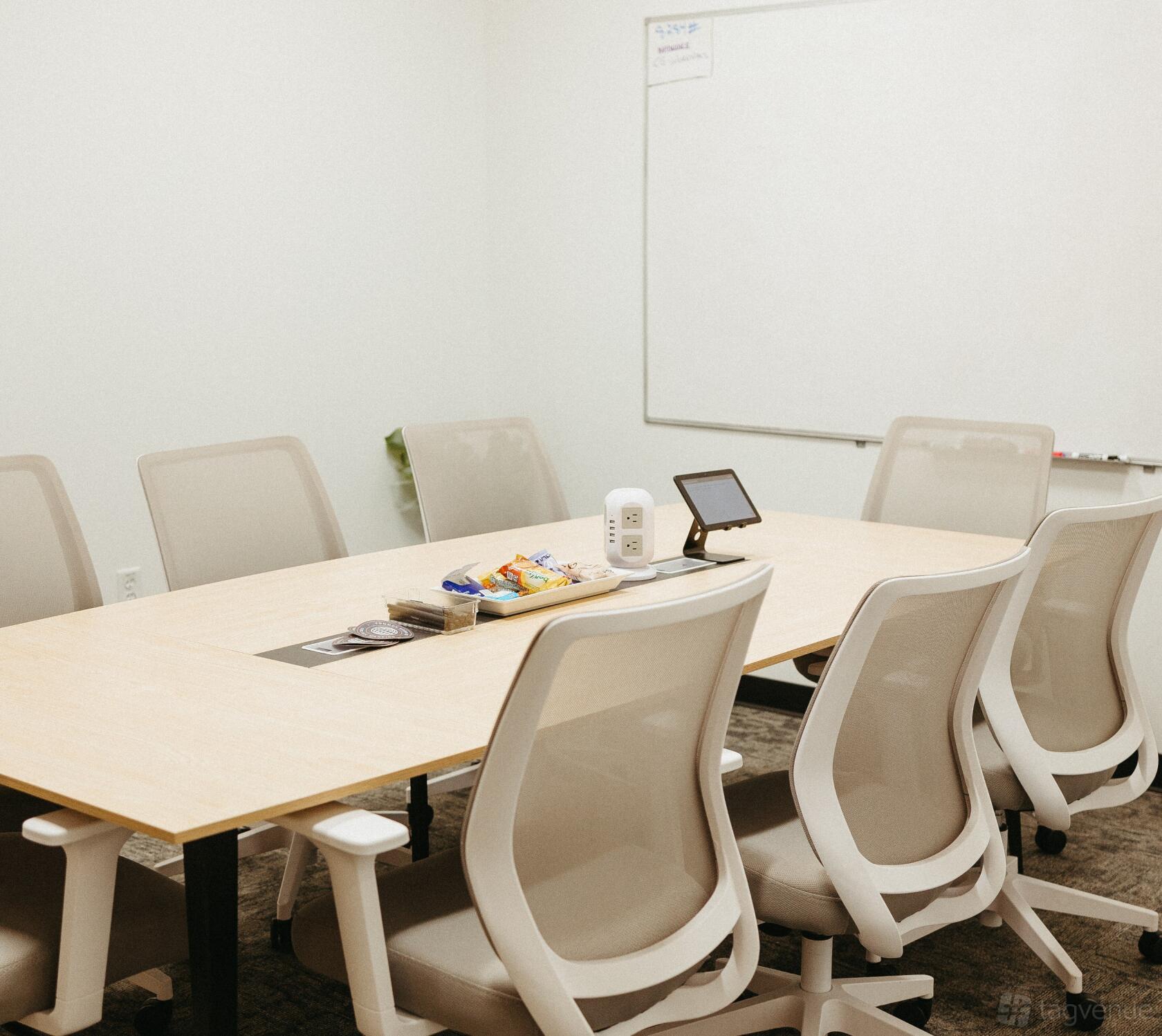 A meeting room with a long wooden table, ergonomic chairs, snacks, and a whiteboard at Common Good Co.