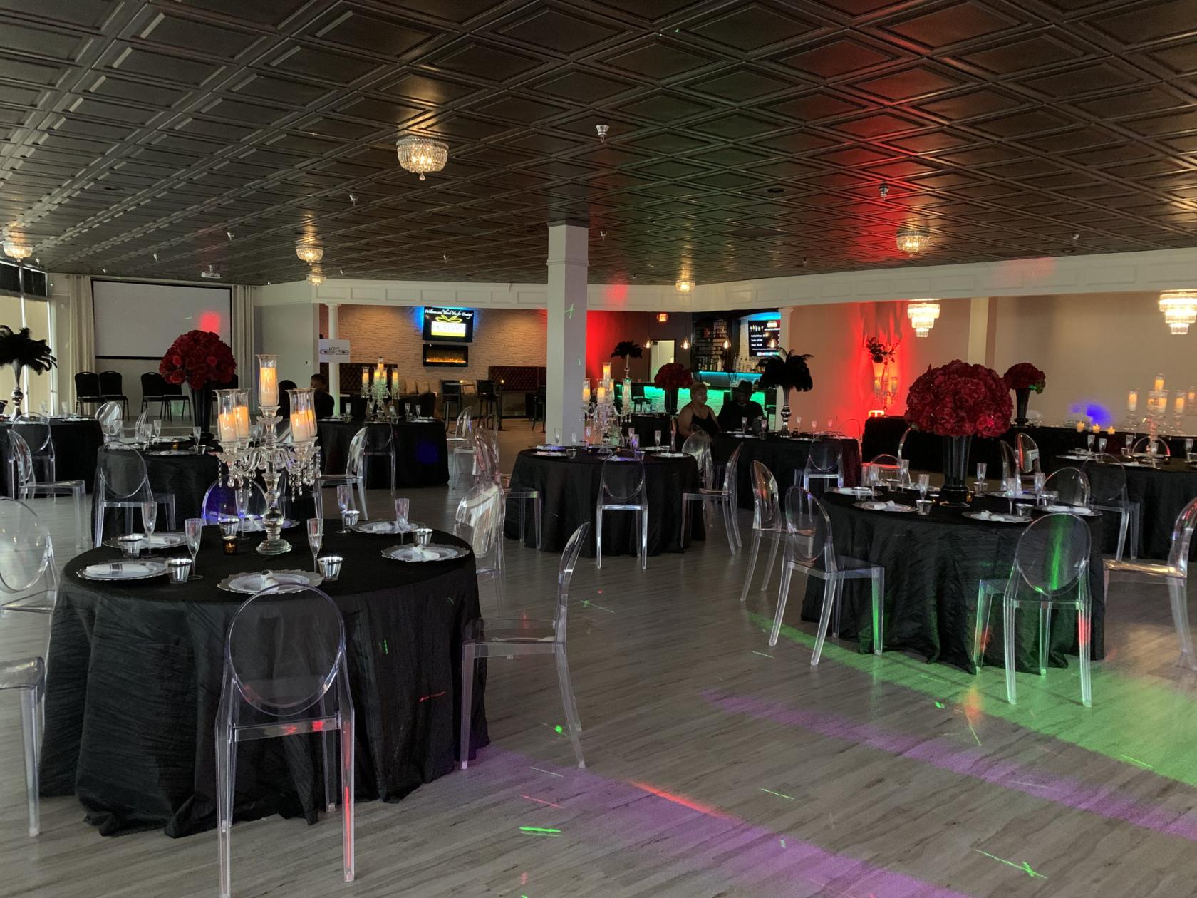 An event venue with black tablecloths, transparent chairs, chandeliers, and accent lighting at Holidays Events Center.