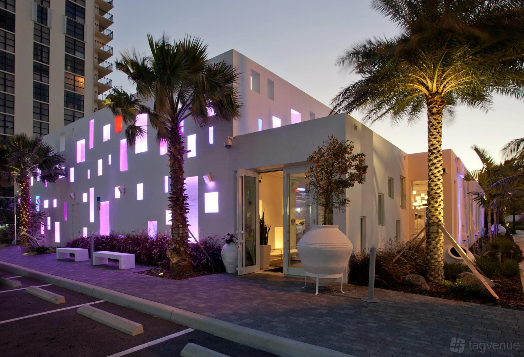 A restaurant with geometric white exterior, illuminated colored windows, palm trees, and modern landscaping at Thasos.