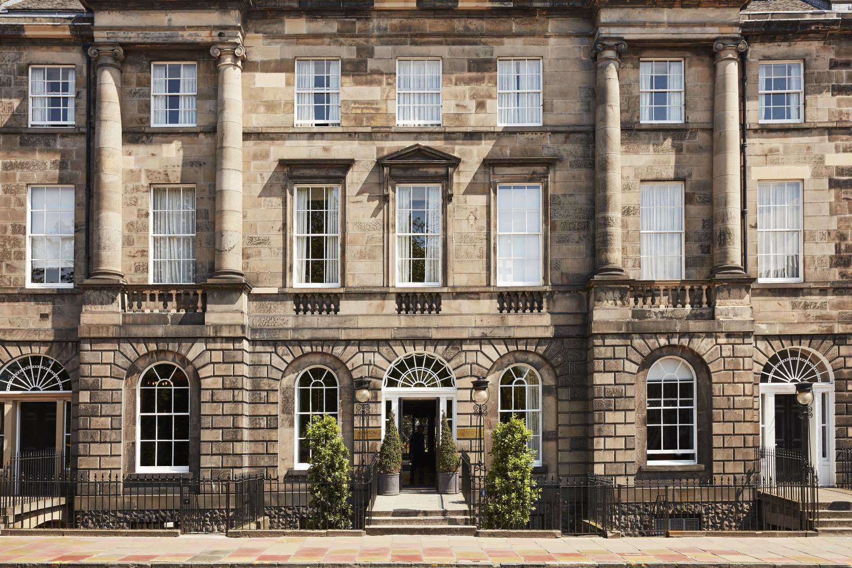 A Georgian hotel exterior with stone facade, tall arched windows, columns, and potted plants at Kimpton Charlotte Square Edinburgh.