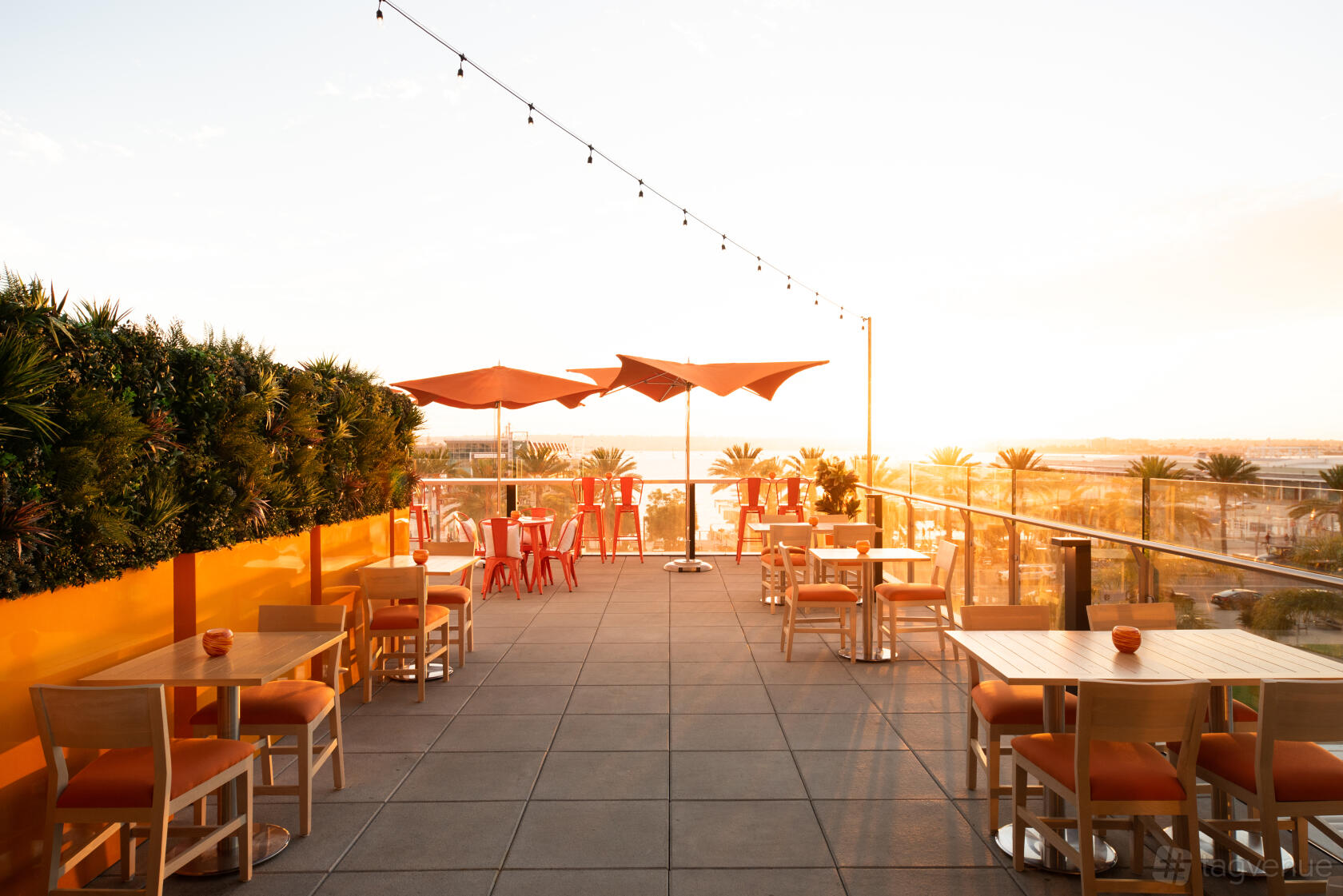 An outdoor restaurant patio with string lights, orange chairs, and tables shaded by large umbrellas at Garibaldi Speakeasy.