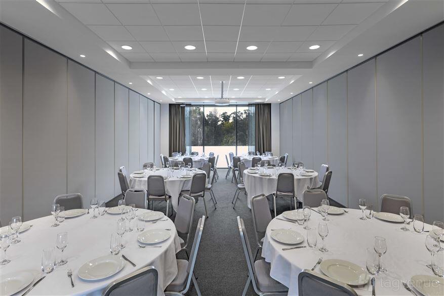 An event space with round tables set with white linens and glassware, large windows and grey walls at Peppers Marysville.