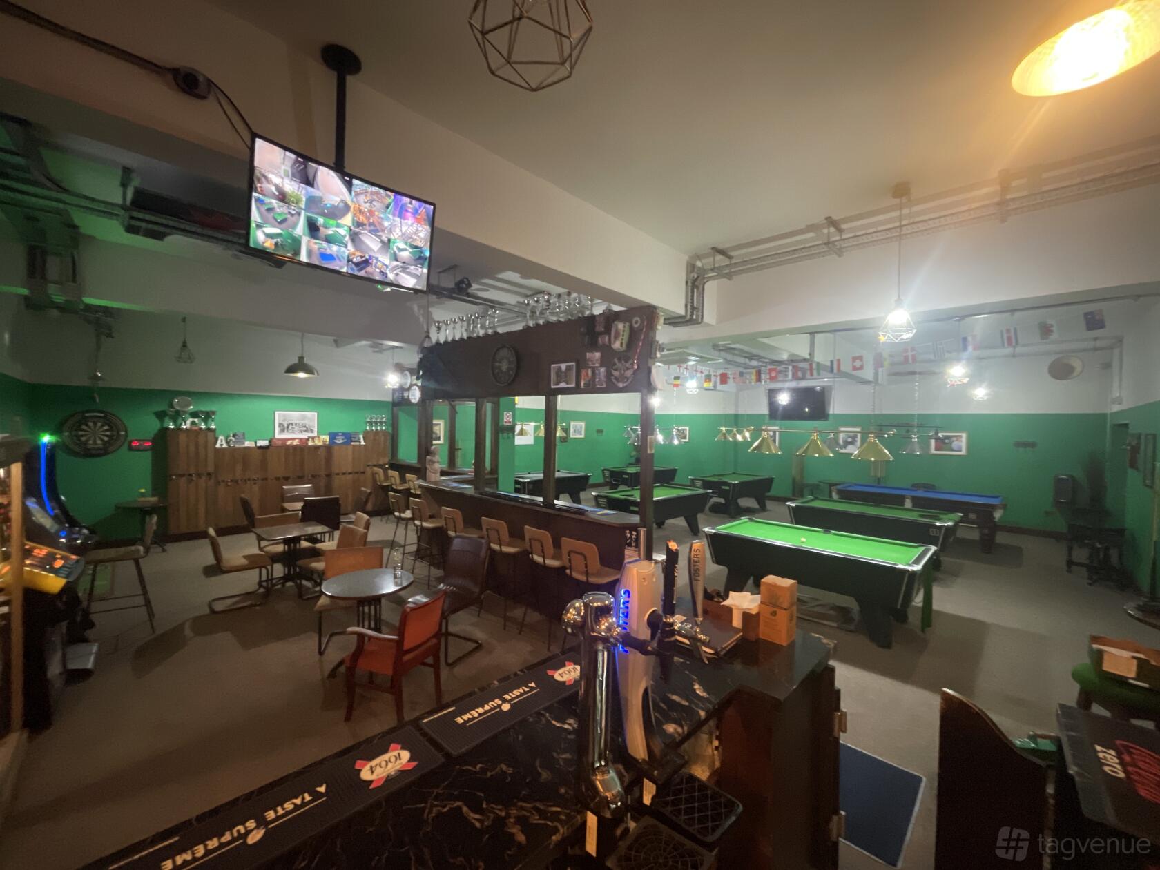A hall in a bar with multiple snooker and pool tables, green walls, and a bar counter at Cousins snooker and pool club.