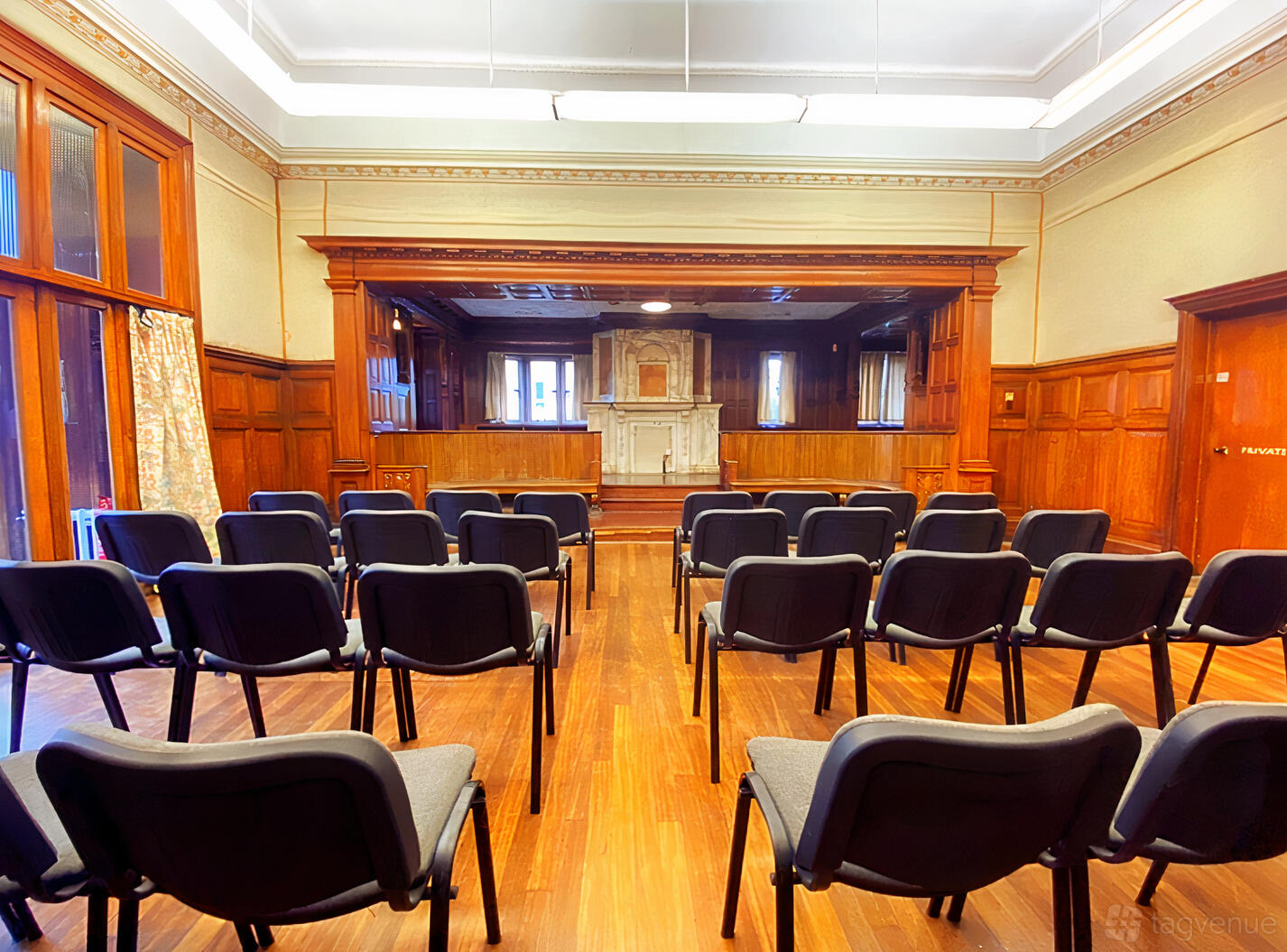 An event venue with wood-paneled walls, a small stage, and rows of chairs in the Billiard Room at Kingswood Arts.