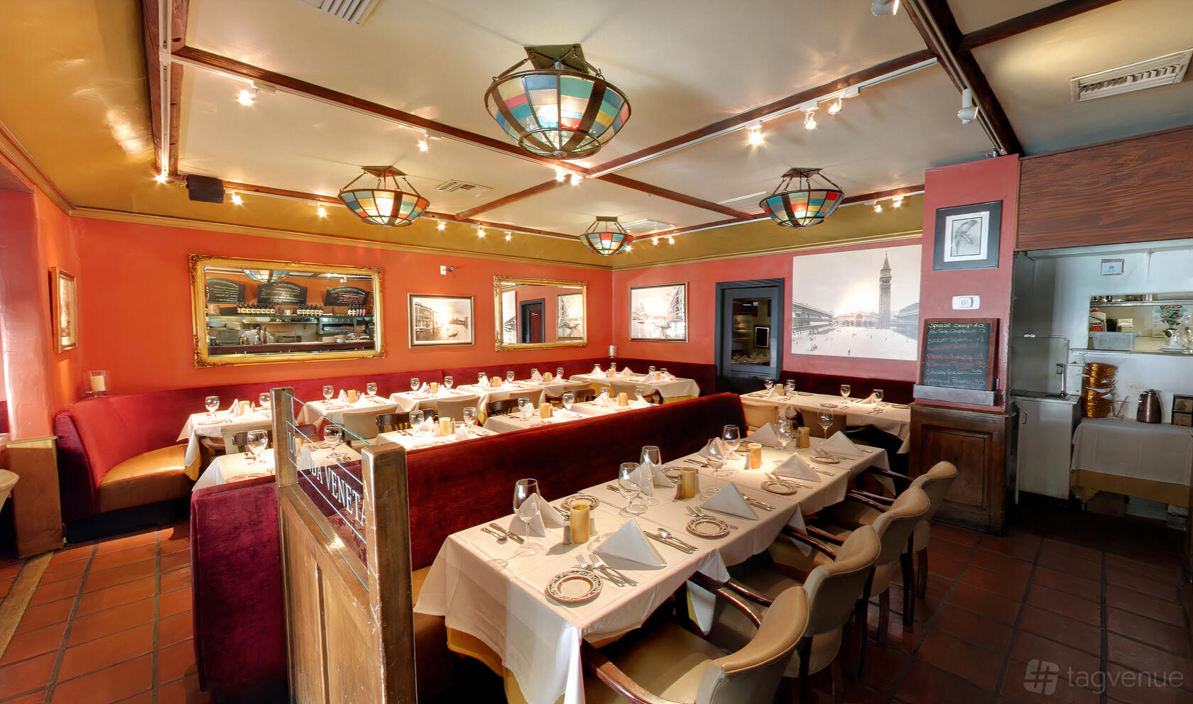 An event space in a restaurant with white tablecloths, red banquettes, and framed art at Locanda Veneta.