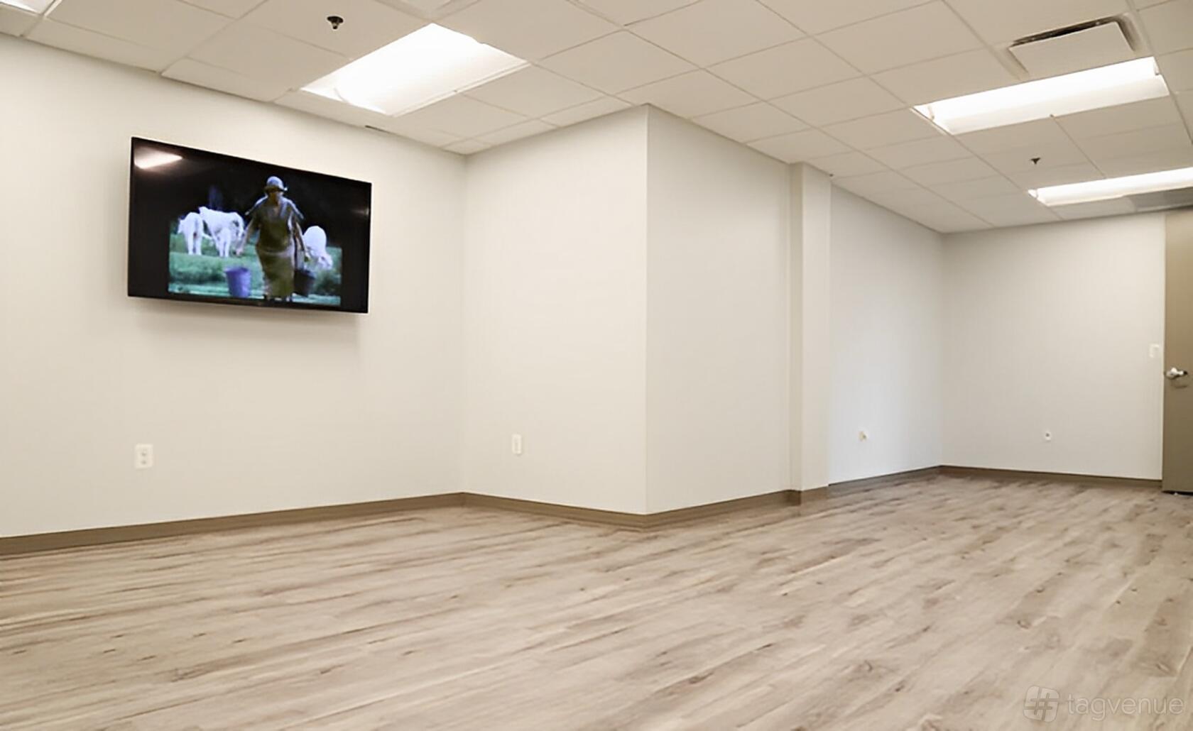 An event space with light wood flooring, white walls, and a wall-mounted TV at Perfect Office Solutions - Silver Spring.