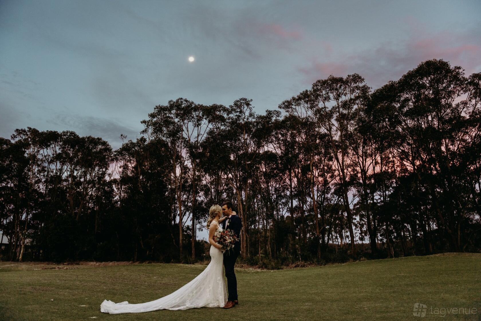 An open grassy event space bordered by tall trees and a twilight sky at The Greenhouse Eatery.