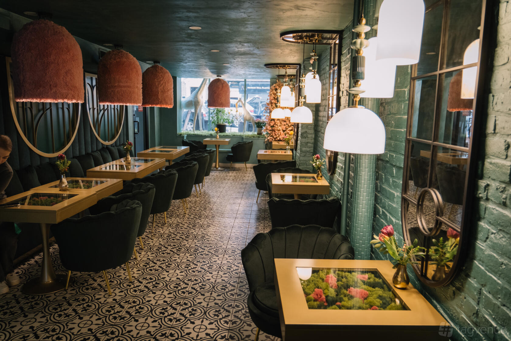 A cafe with patterned tile floors, green velvet seating, glass-top tables, and hanging lamps at Sahola Coffee.