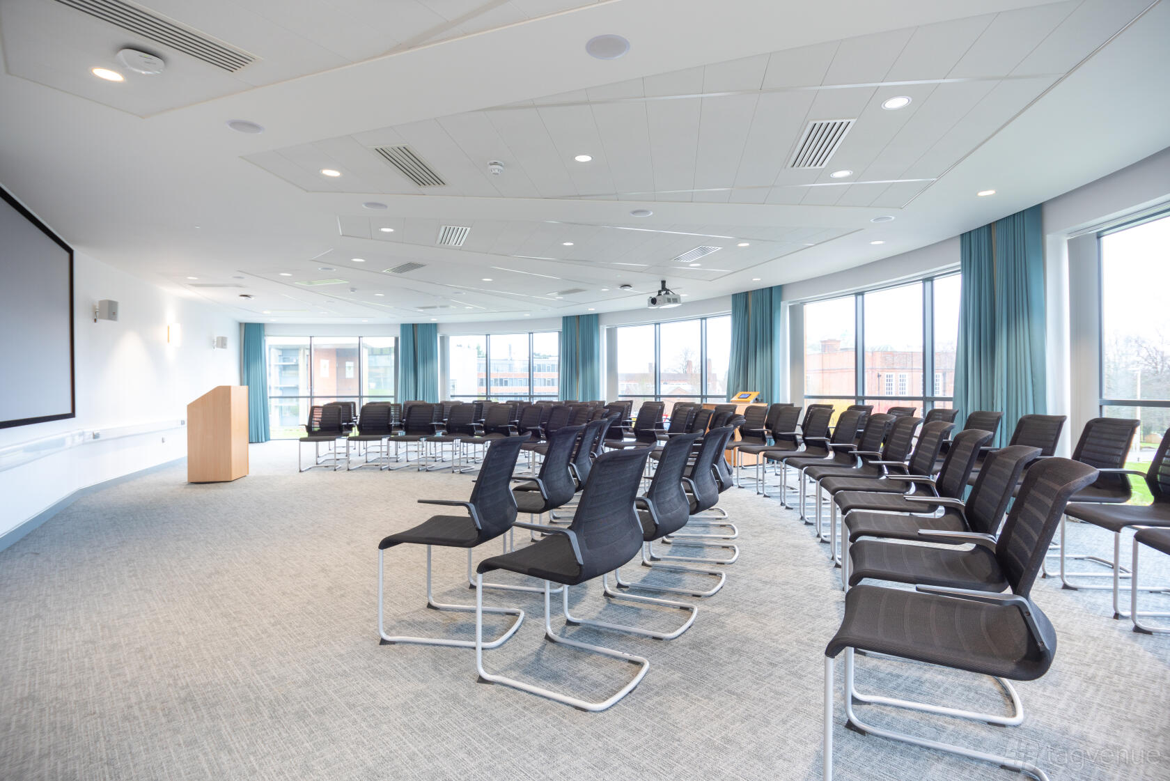 A conference centre with rows of black chairs, floor-to-ceiling windows, and a podium at Rothamsted Conference Centre.