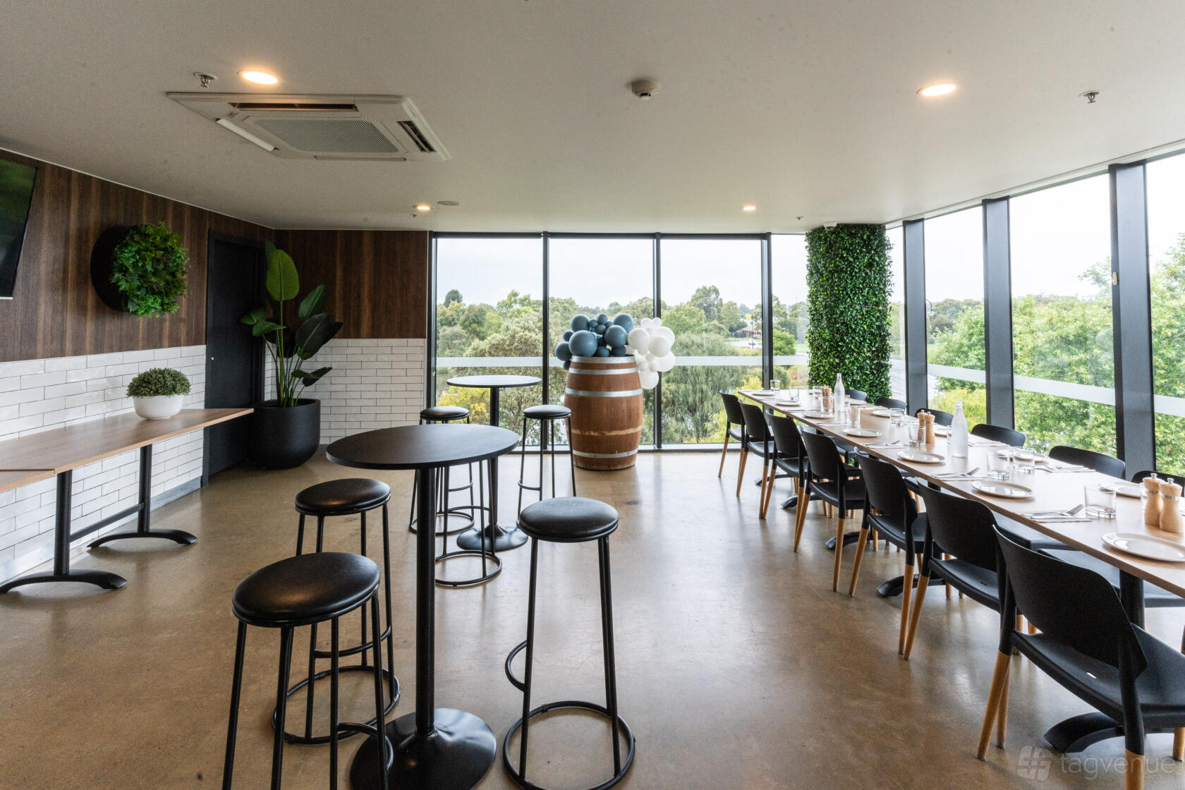A function room with floor-to-ceiling windows, long banquet tables, and greenery accents at Slices Doreen.