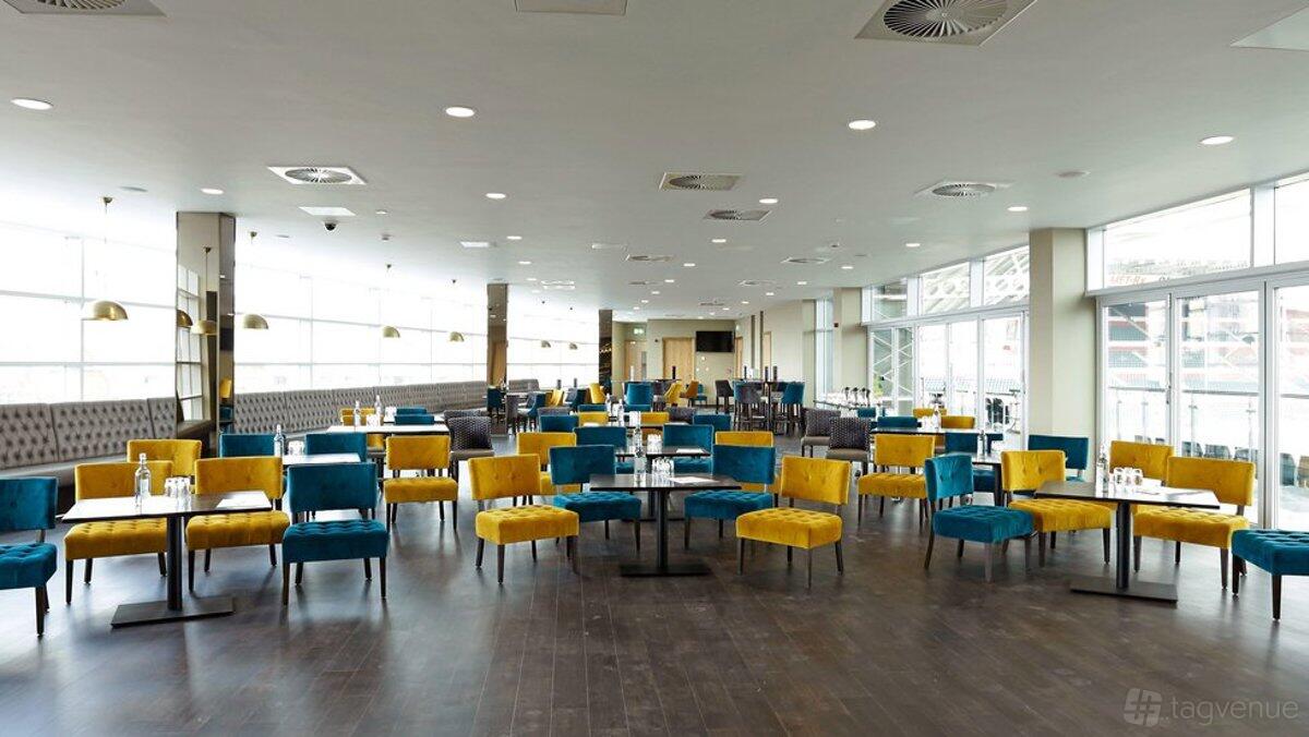 An event space with yellow and blue chairs, dark wood floors, and large windows at Leicester Tigers The Clubhouse.