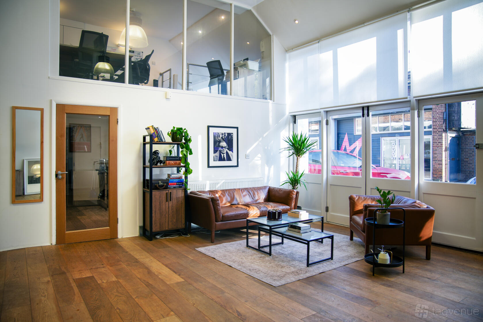 A photo studio with high ceilings, large windows, leather seating, and wood floors at Spacious West London Photo Studio with Office.