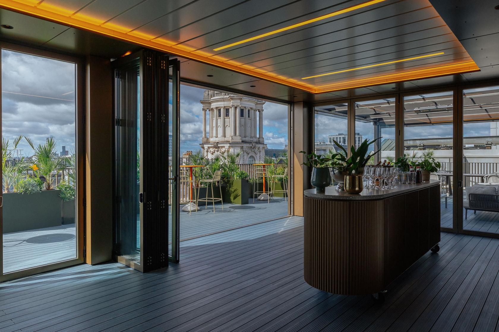 A rooftop terrace with glass doors, potted plants, and city views at Uncommon Holborn